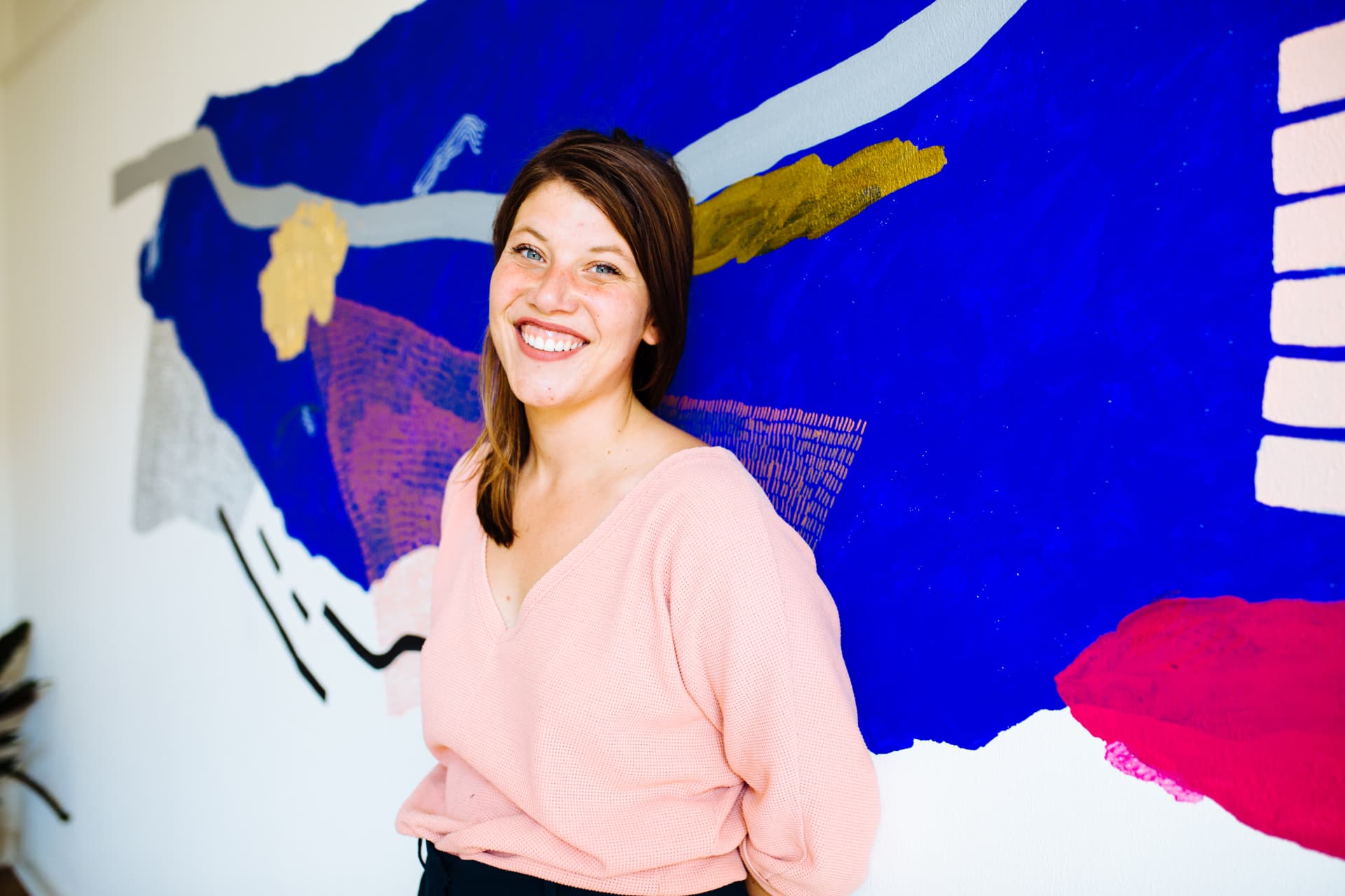 Tessa lachend voor een kleurrijke muurschildering